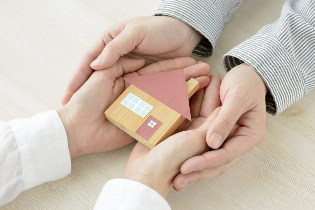 mains qui se touche avec maison en bois miniature