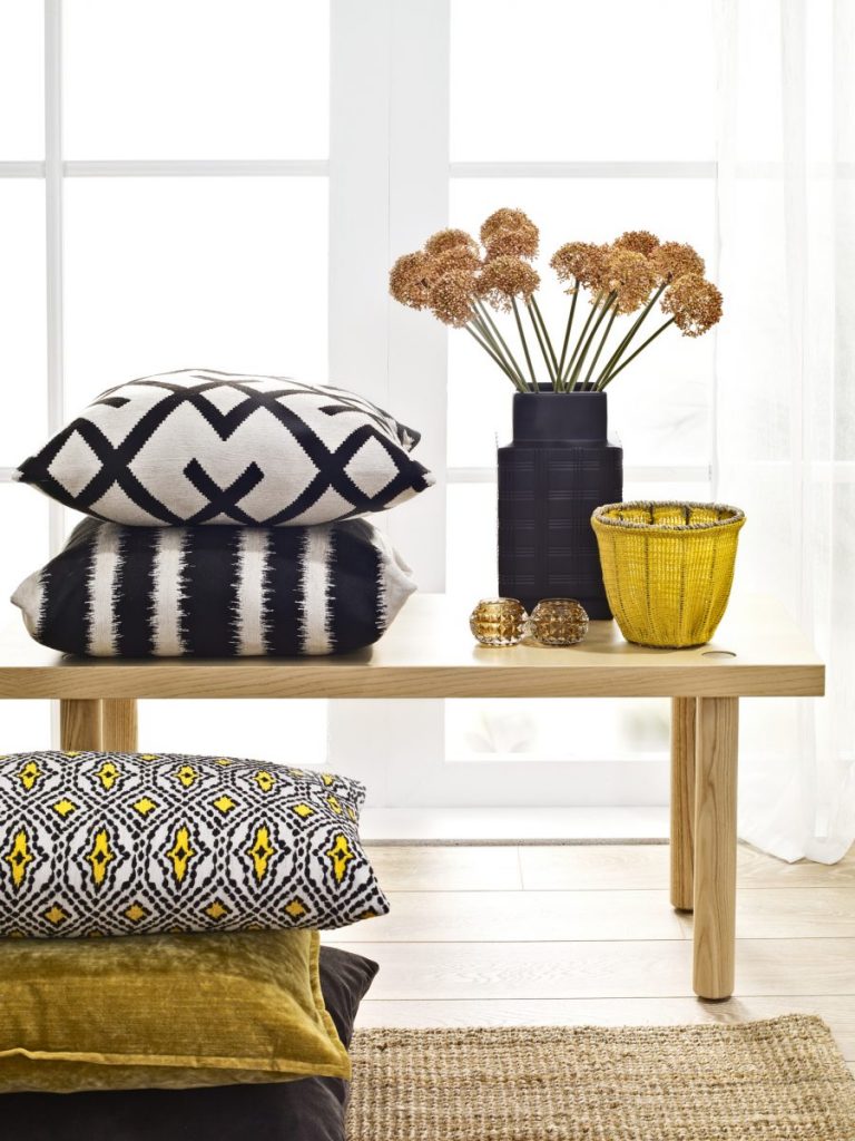 banc en bois avec vase de fleurs séchées et coussin jaune noir et blanc