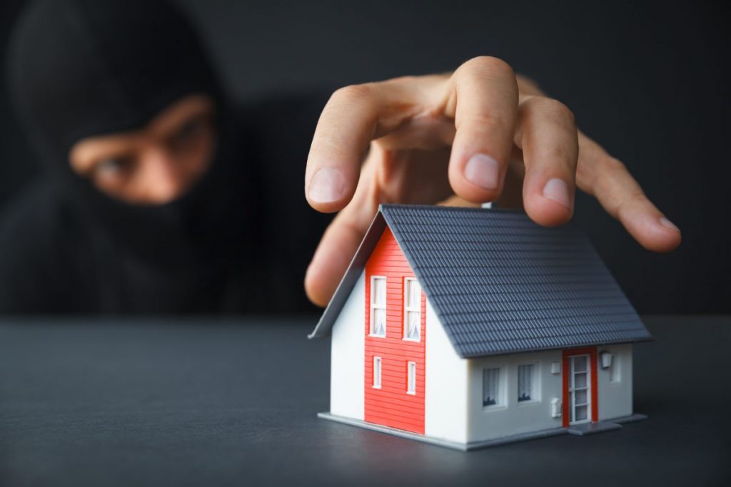 cambrioleur avecmain au dessus d'une petite maquette de maison rouge et blanche