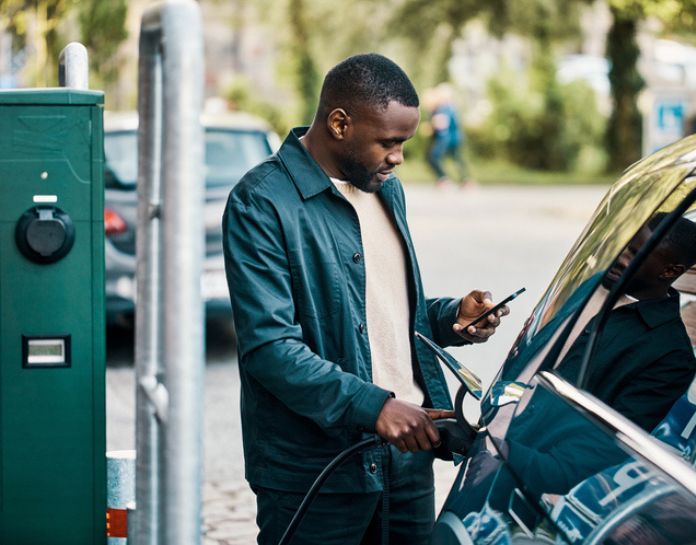 homme regarde son telephone en rechargeant sa voiture electrique