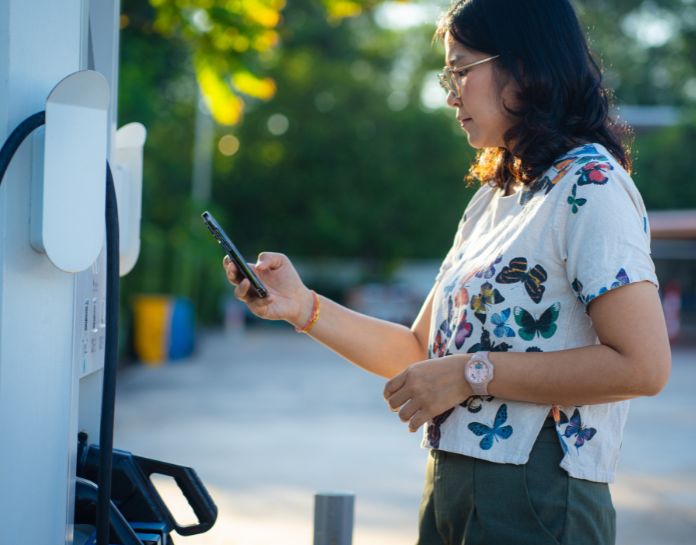 femme recharge son vehicule sur borne publique avec smartphone en main